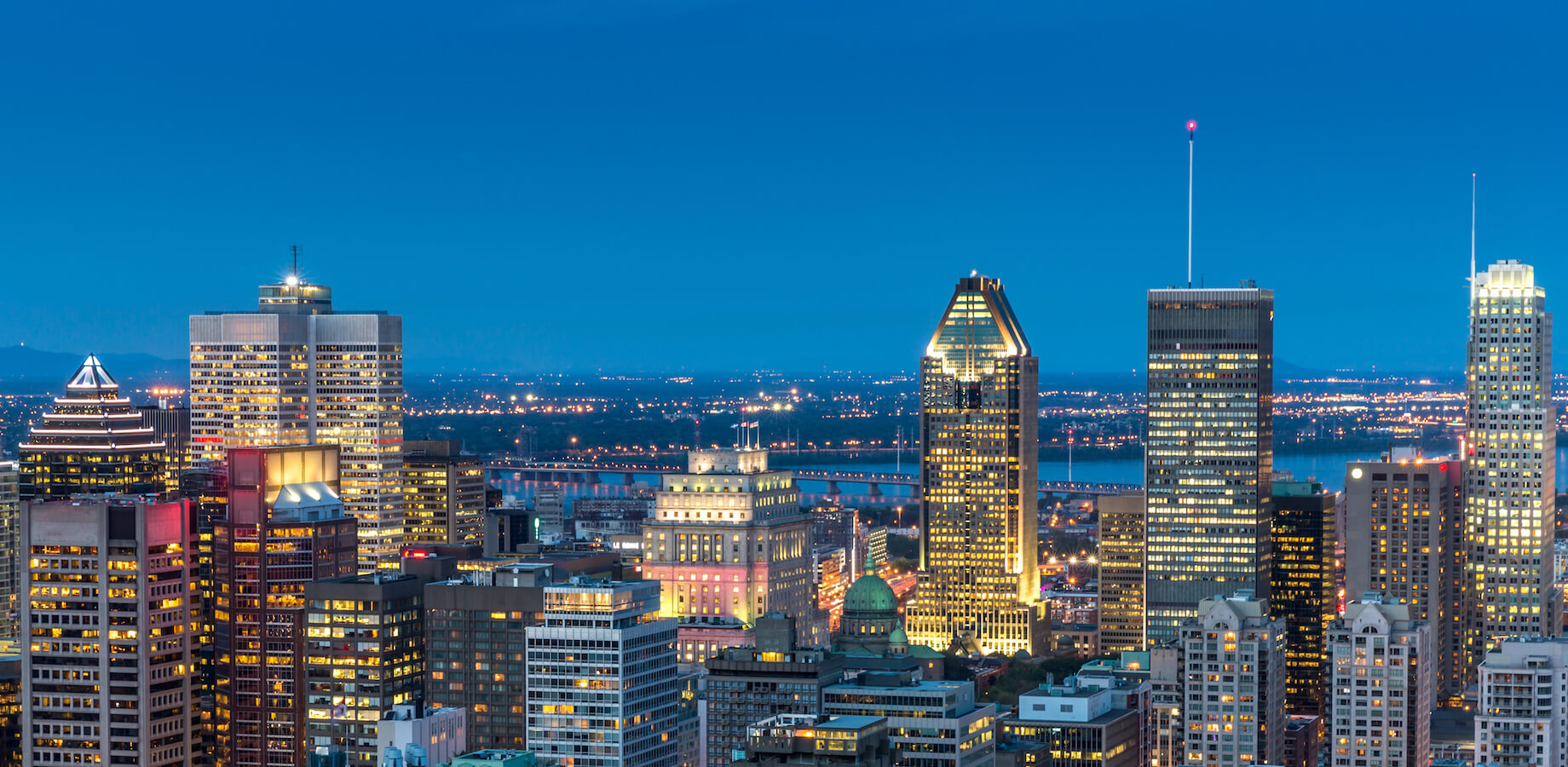 Vue du centre-ville de Montréal, de ses gratte-ciel, du pont Jacques-Cartier et du fleuve Saint-Laurent à l'heure bleue